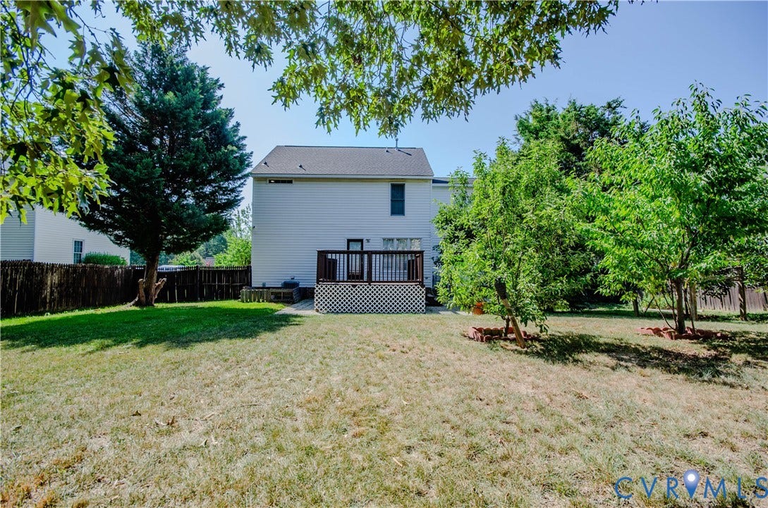 Expansive backyard featuring a wood deck with lattice skirting, mature trees, and a privacy fence