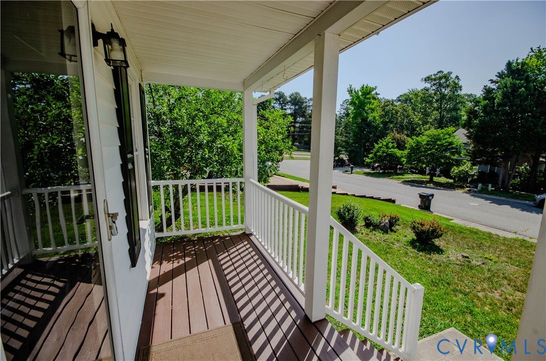 Covered front porch with white railings, brown wood-finish flooring, and exterior lighting fixture