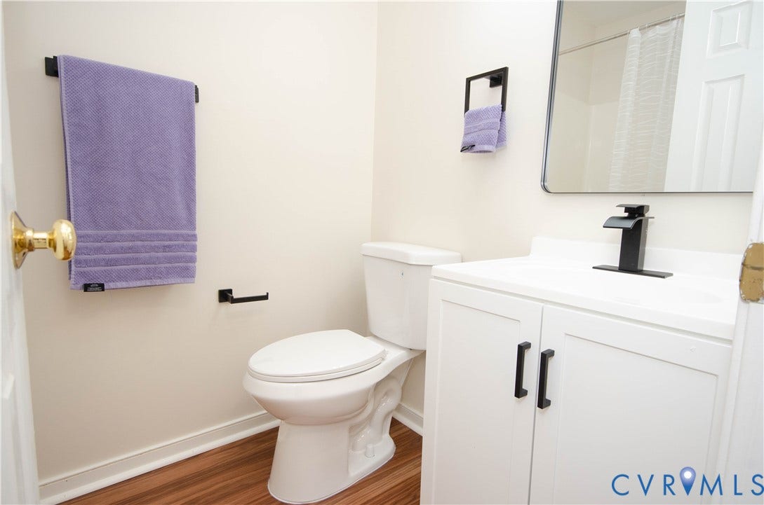 White vanity with matte black hardware, white countertop, matte black faucet, wood-finish flooring, and a wall-mounted mirror