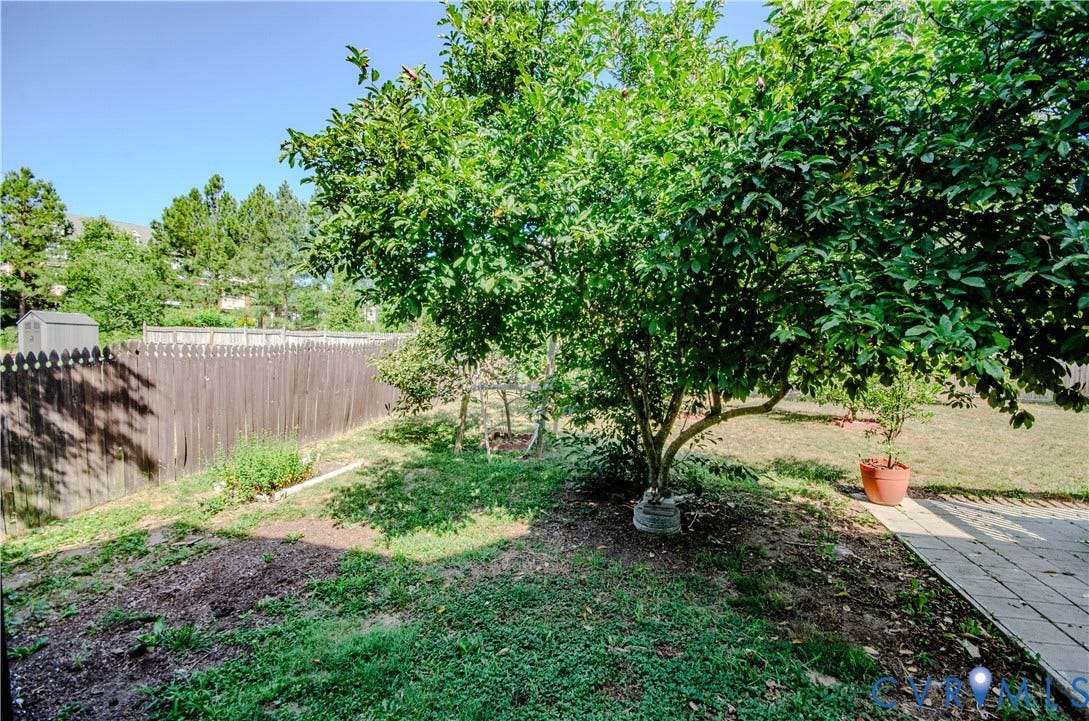 Fenced backyard featuring a mature tree, stone paver patio, and a storage shed
