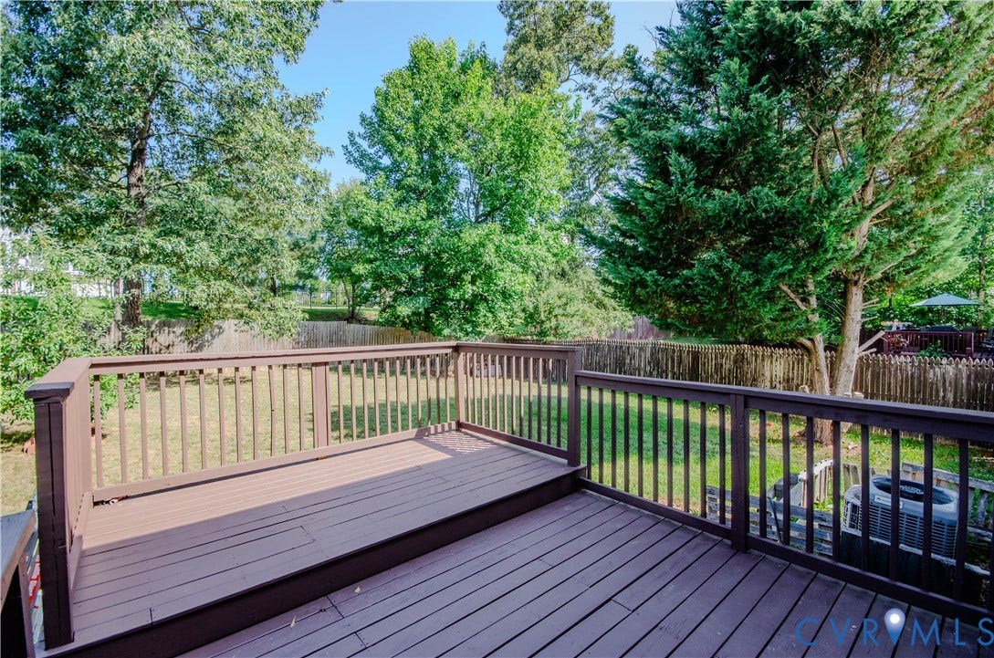 Expansive exterior deck featuring wood-finish decking and railing, overlooking a fenced backyard with mature trees