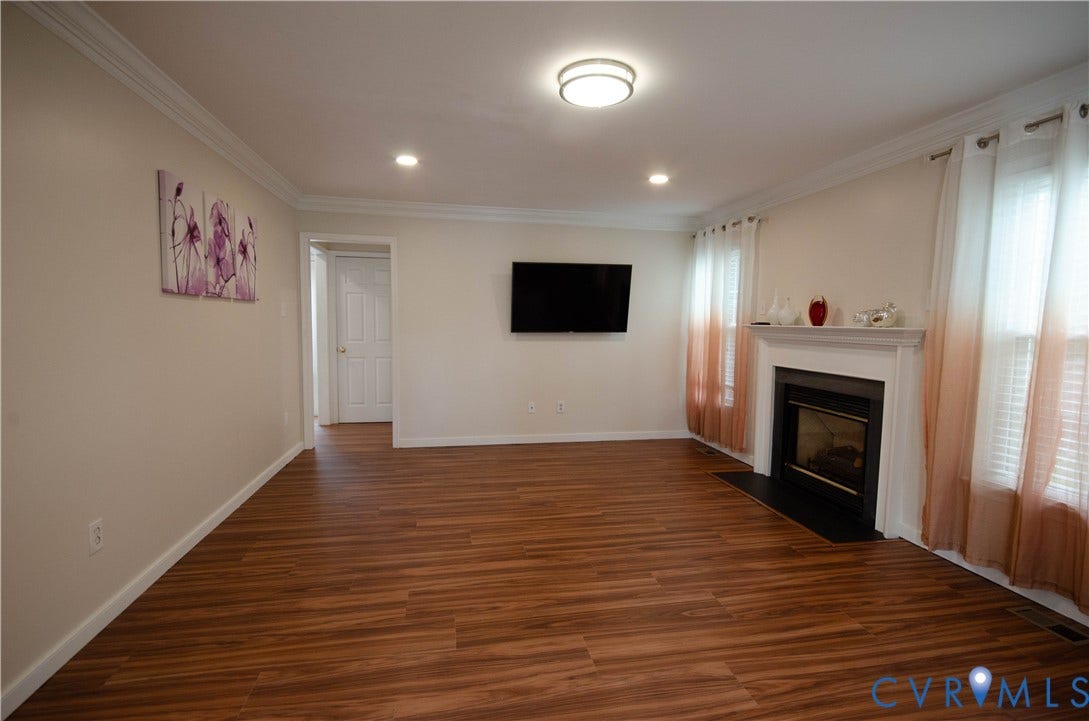 Wood-finish flooring, crown molding, recessed lighting, ceiling-mounted light fixture, and a fireplace with a white mantel and black hearth