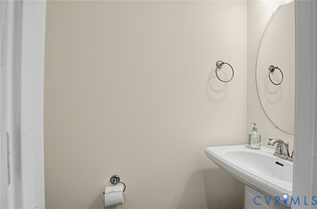 Pedestal sink with chrome faucet, oval mirror, and neutral wall tones