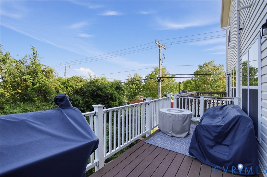 Outdoor deck with composite wood-finish flooring, white spindle railing, and a window with exterior lighting