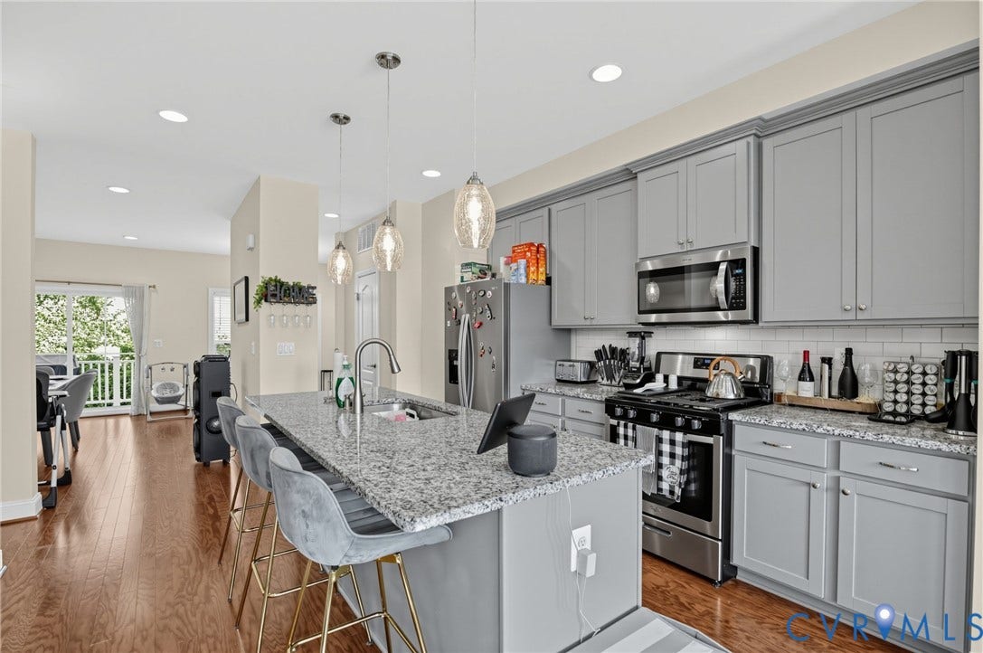 Kitchen featuring a central island with countertop seating, stainless steel appliances, pendant lighting, shaker-style cabinetry, and wood-finish flooring