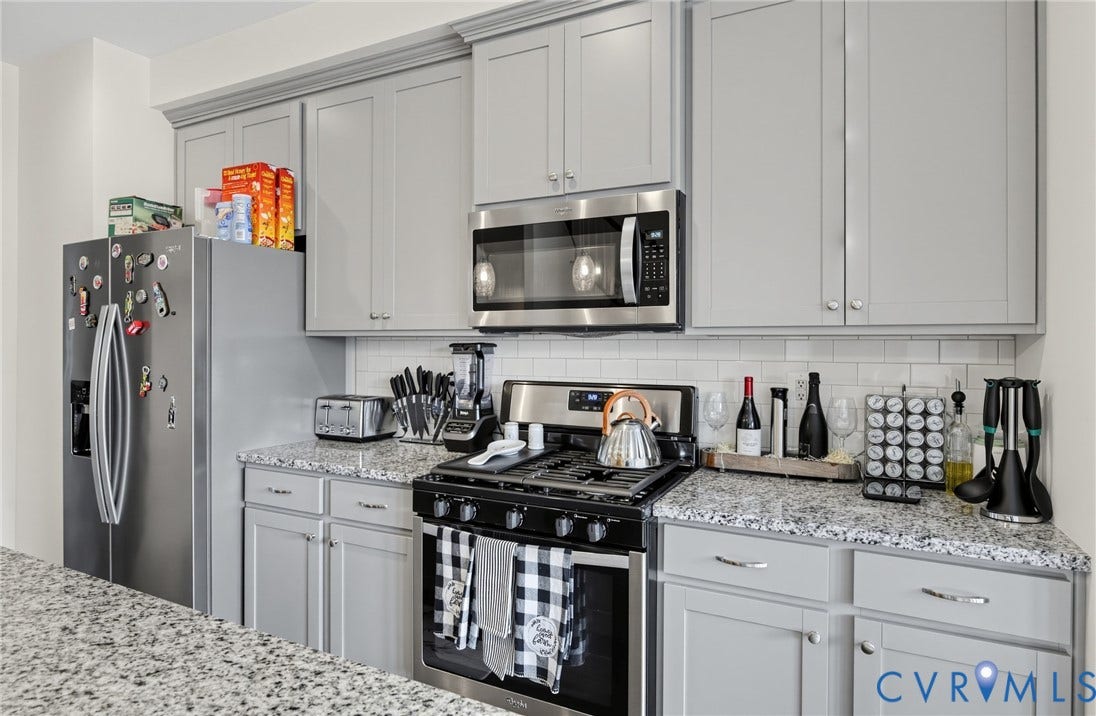 Kitchen featuring light gray cabinetry, stainless steel appliances, granite countertops, and a subway tile backsplash