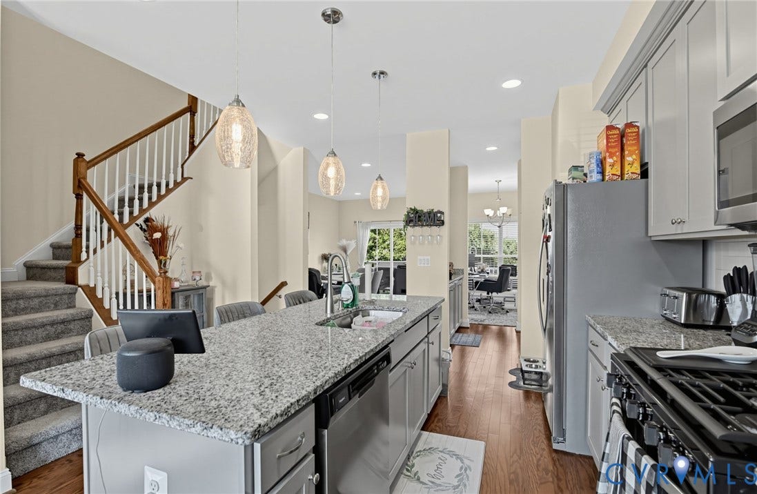 Kitchen featuring a large island with a sink, stainless steel appliances, grey cabinetry, and wood-finish flooring