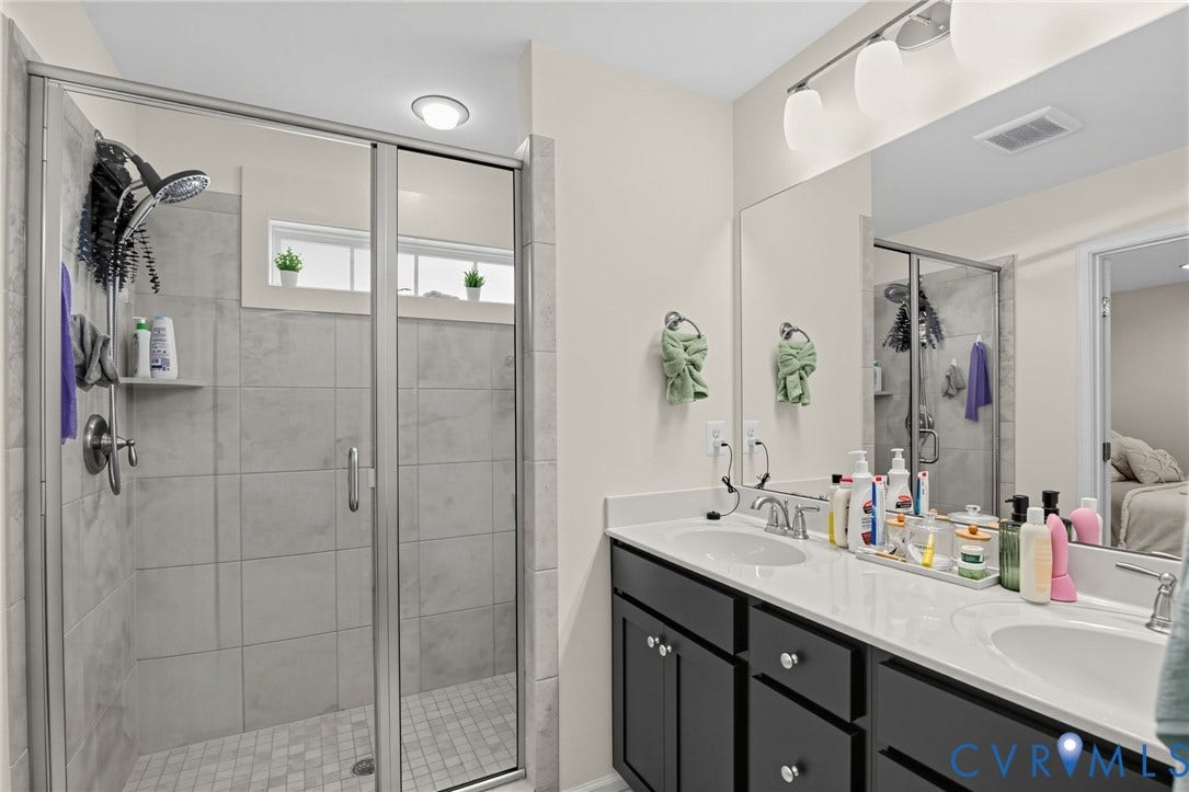 Dual vanity with integrated sinks and dark cabinetry, a large frameless mirror, and a three-light fixture