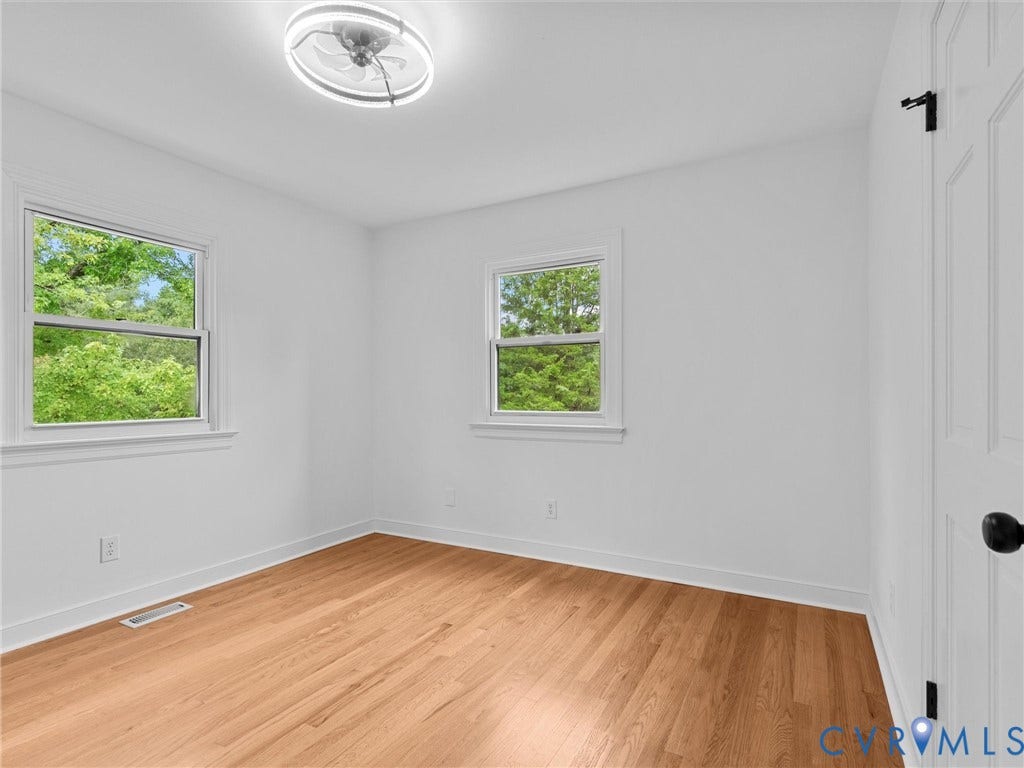 7361 Creekridge Road, Henrico, VA 23231 Bright room with wood-finish flooring, two large windows, a ceiling-mounted light fixture, and a paneled door with matte black hardware