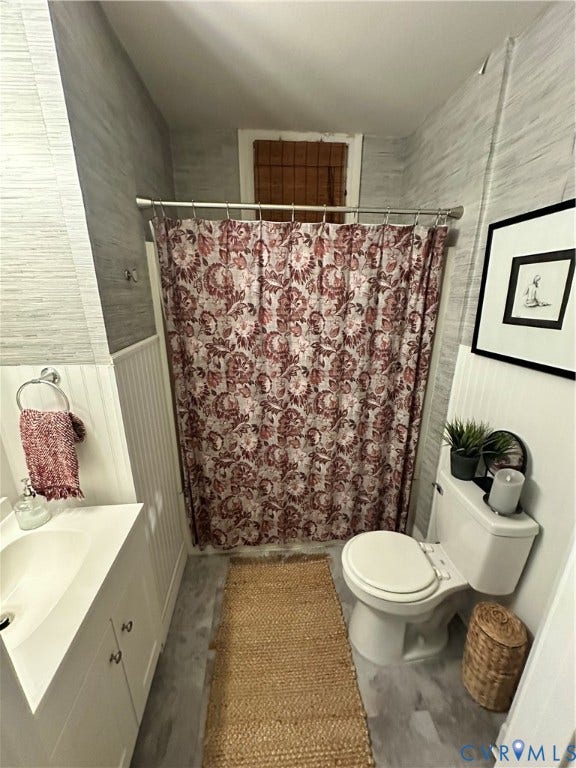 White vanity with integrated sink, paneling on lower walls, textured wall covering, and a window with blinds