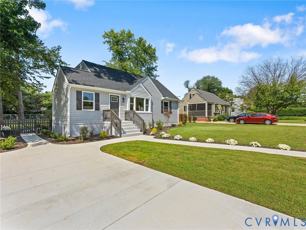 Exterior featuring light gray siding, dark gray roof, front entry steps, a paved driveway, and a manicured lawn