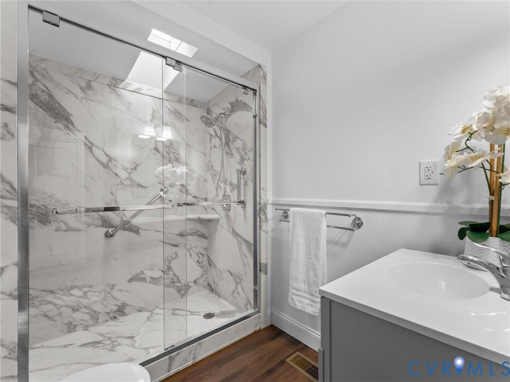 Shower featuring glass enclosure, built-in shelving, and marble-finish walls