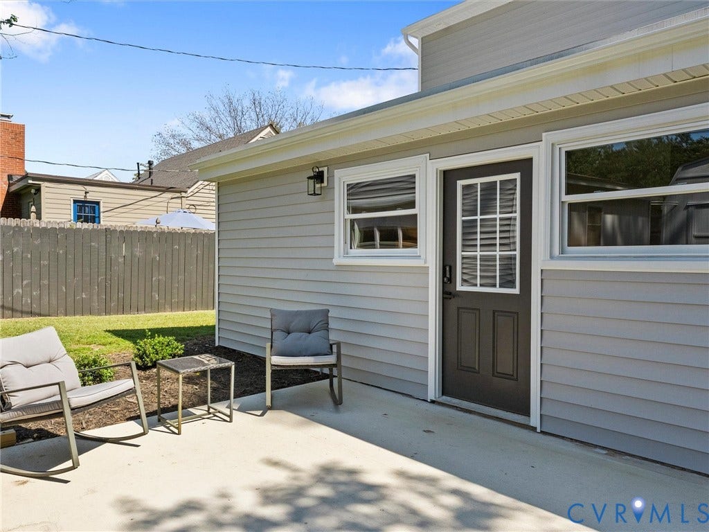 Exterior featuring gray siding, a black paneled door with grid-pane windows, white-framed windows, and an outdoor light fixture