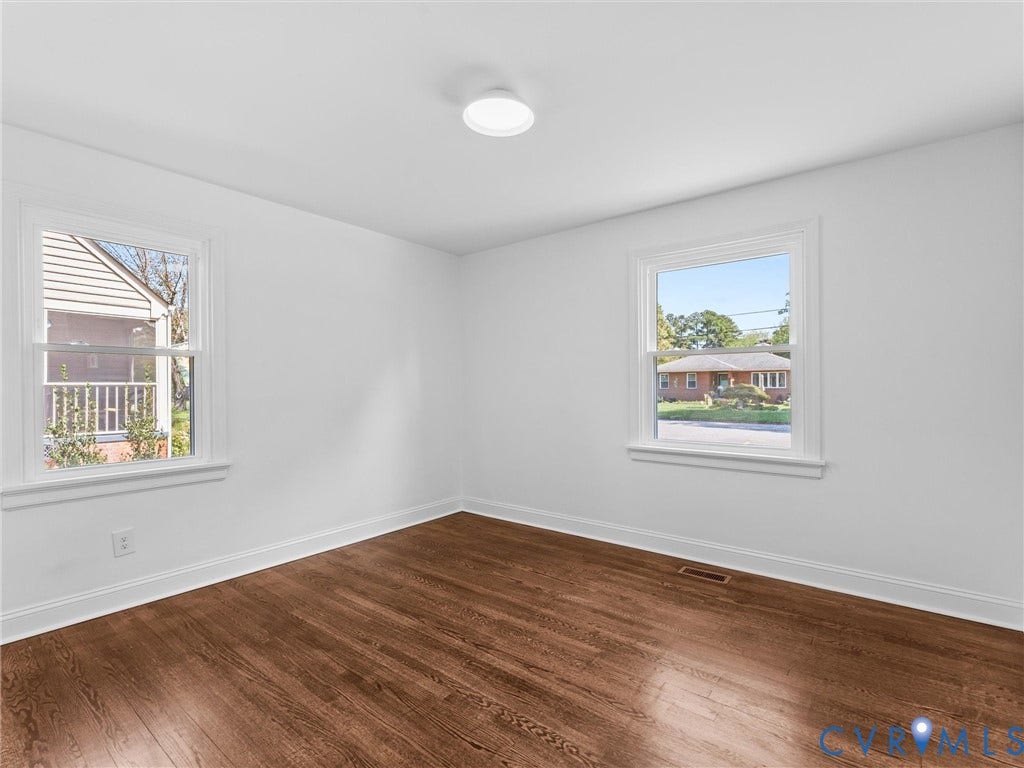 Hardwood flooring, white walls, two windows with white trim, and a ceiling-mounted light fixture