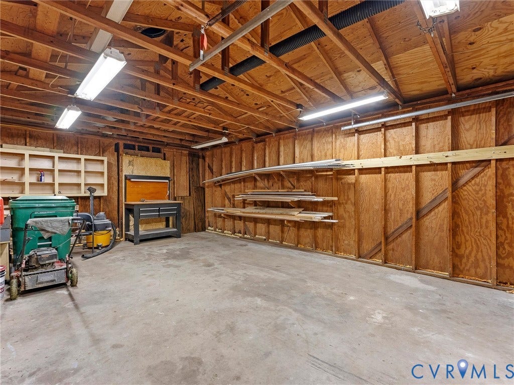 Concrete flooring with built-in wooden shelving, exposed wood beam ceiling, and fluorescent lighting