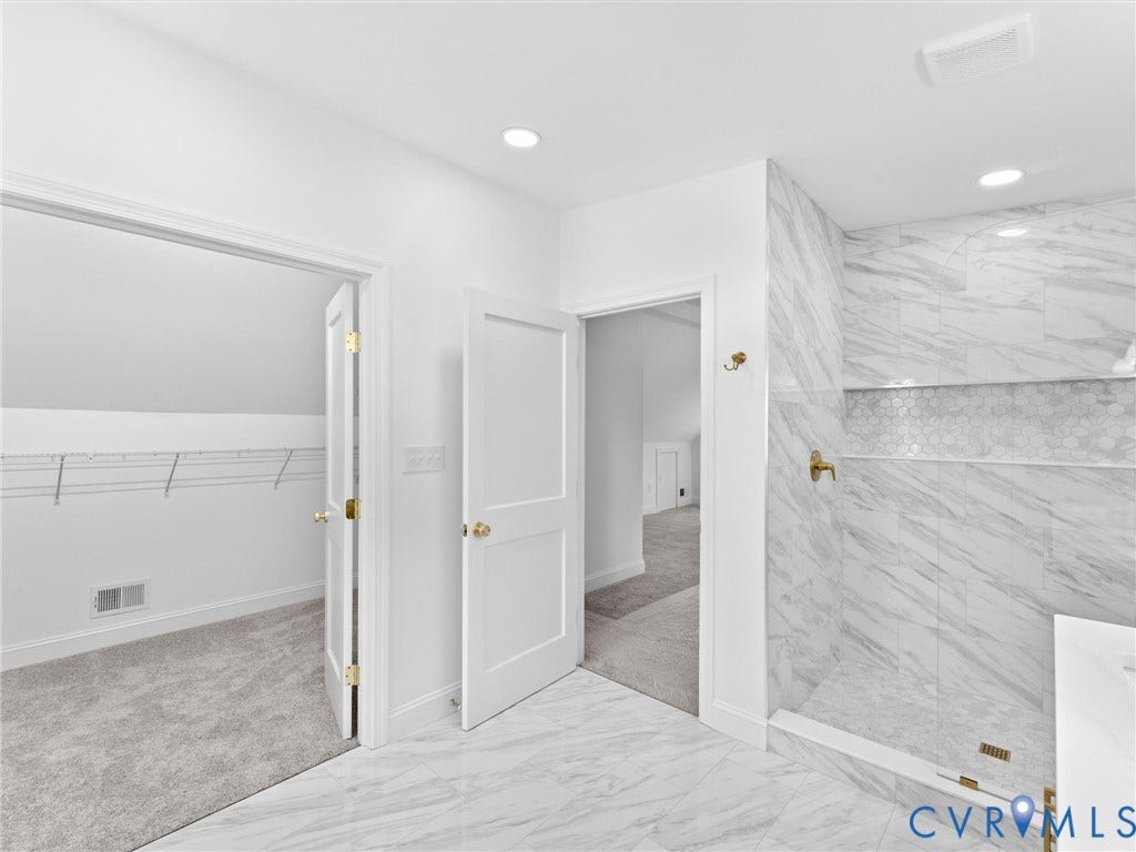 White tile flooring, walk-in shower with marble-look wall tile, built-in shower niche, and gold-toned fixtures