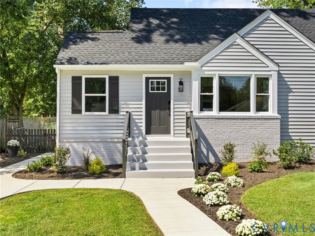 Light gray siding exterior with a dark gray front door, flanked by a contemporary sconce and dark shutters