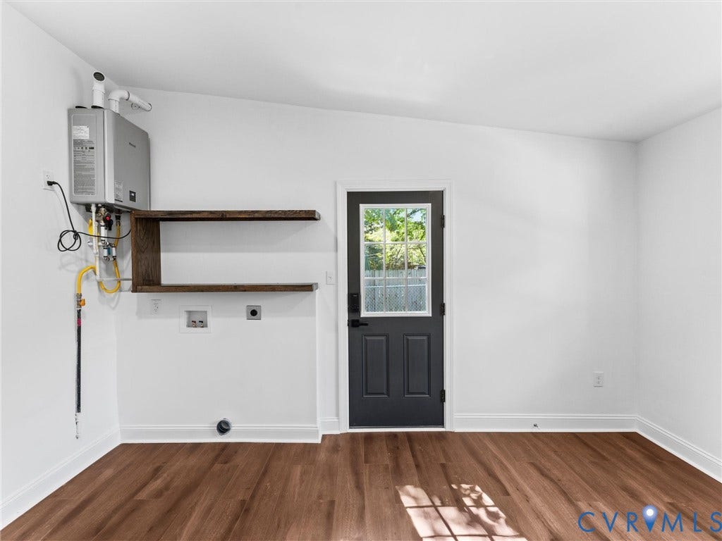 Wood-finish flooring, white walls, dark-paneled exterior door with window, tankless water heater, and built-in wood shelves