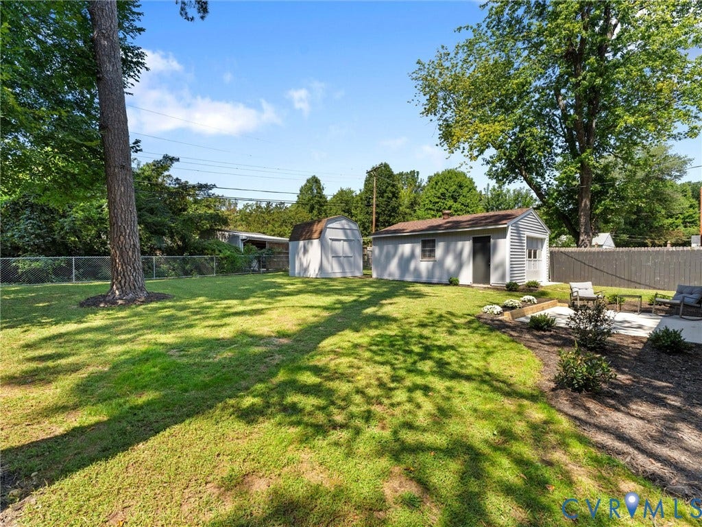 Expansive green space featuring two detached utility buildings, a paved patio, and mature trees