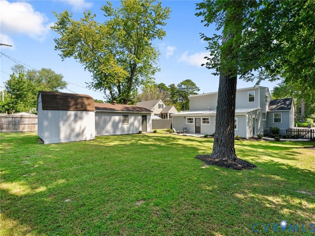 Expansive green lawn with mature trees, a detached storage shed, and a fenced area