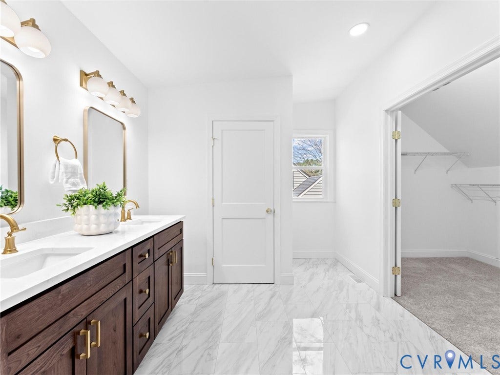 Dual vanity with white countertop, rich wood cabinetry, gold-tone hardware, and elegant wall-mounted lighting
