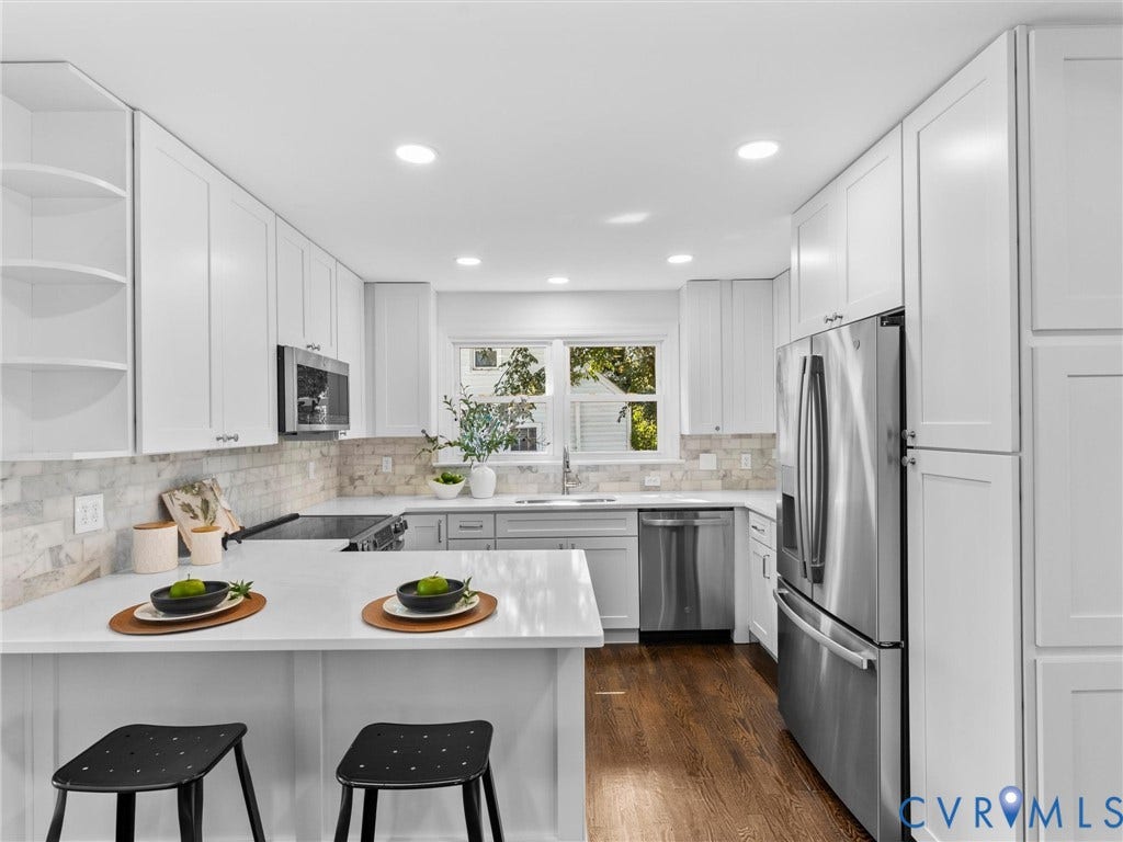 White shaker cabinetry, stainless steel appliances, light-toned countertops, tile backsplash, and wood-finish flooring