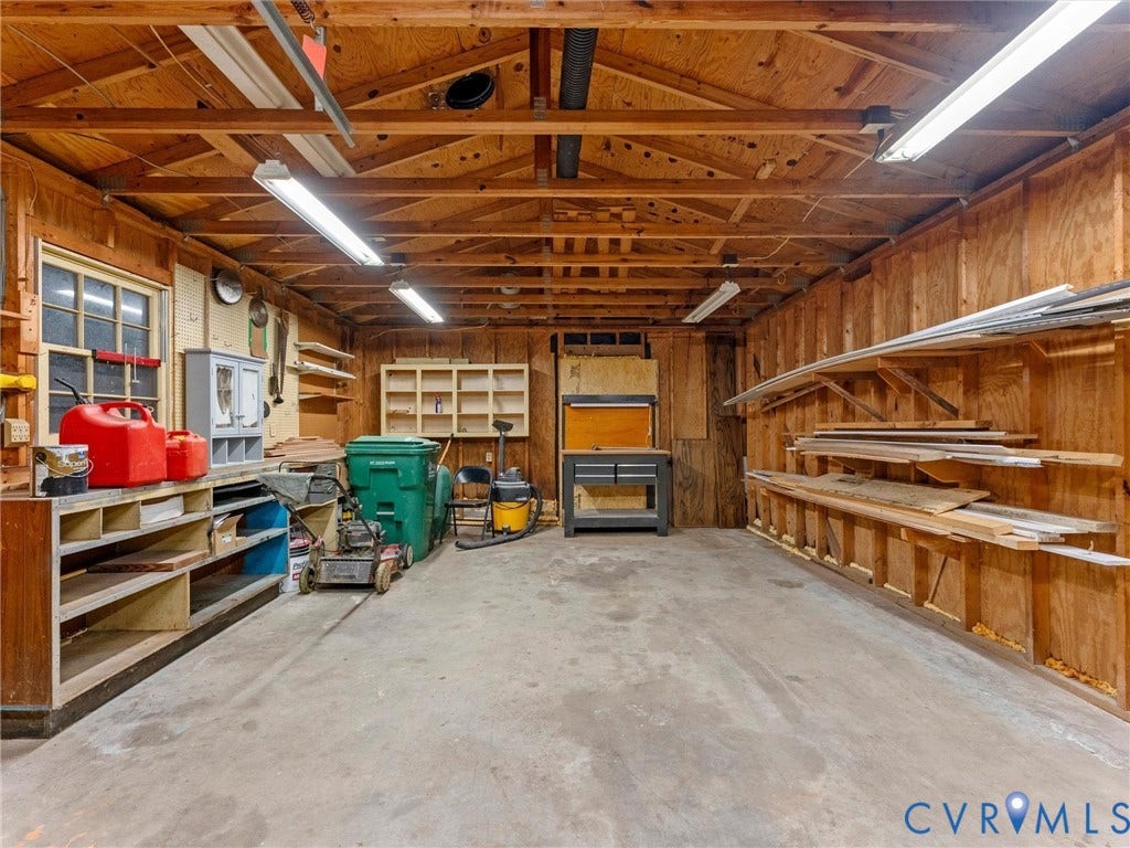 Spacious garage with exposed wood beam ceiling, concrete flooring, wood paneling, built-in shelving, and a multi-pane window