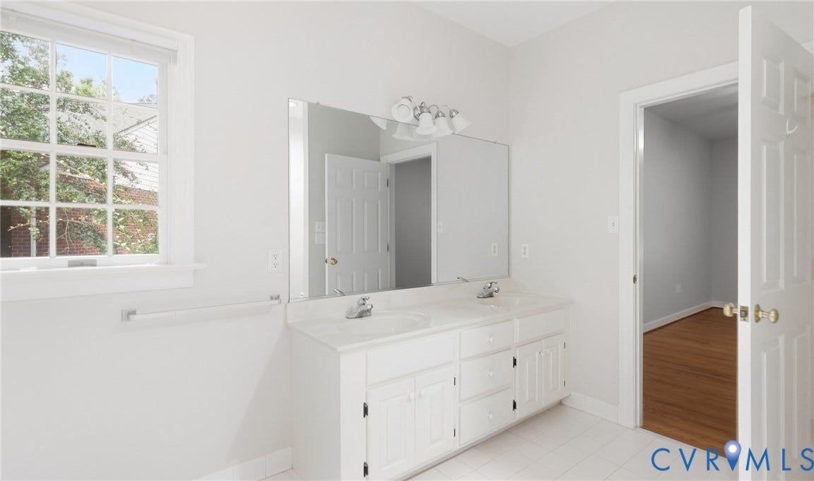 5500 Lakemere Drive, 55+ Community, North Chesterfield, VA 23234 Dual vanity with white cabinetry and integrated sinks, complemented by a large wall-mounted mirror and overhead sconce lighting