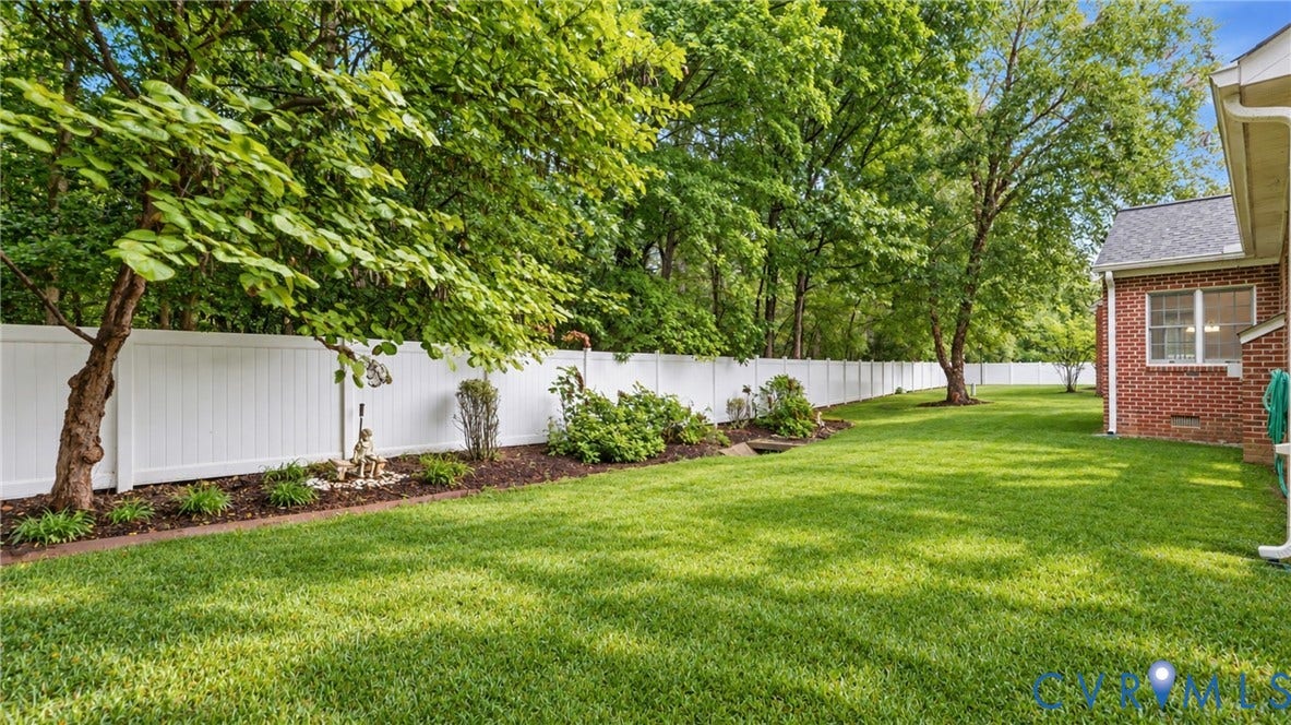 5500 Lakemere Drive, 55+ Community, North Chesterfield, VA 23234 Expansive green lawn, white privacy fence, mature trees, landscaped garden beds, and a brick exterior