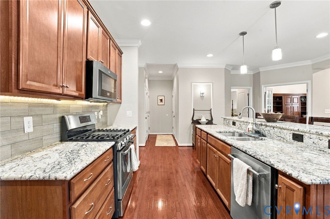 Wood-finish cabinetry, stainless steel appliances, granite countertops, tile backsplash, and wood-finish flooring
