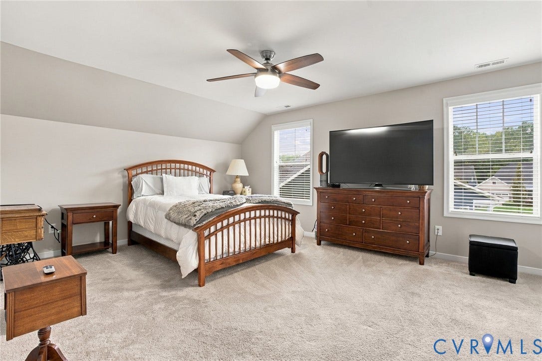 Spacious room with sloped ceilings, light-colored carpeting, multiple windows, and a ceiling fan