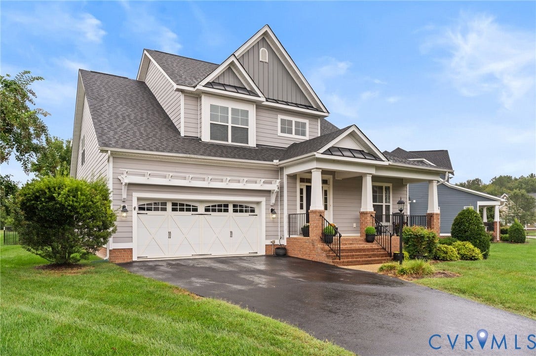 Two-story residence featuring siding and brick facade, an attached two-car garage with decorative doors, a covered front porch with columns, and a paved driveway