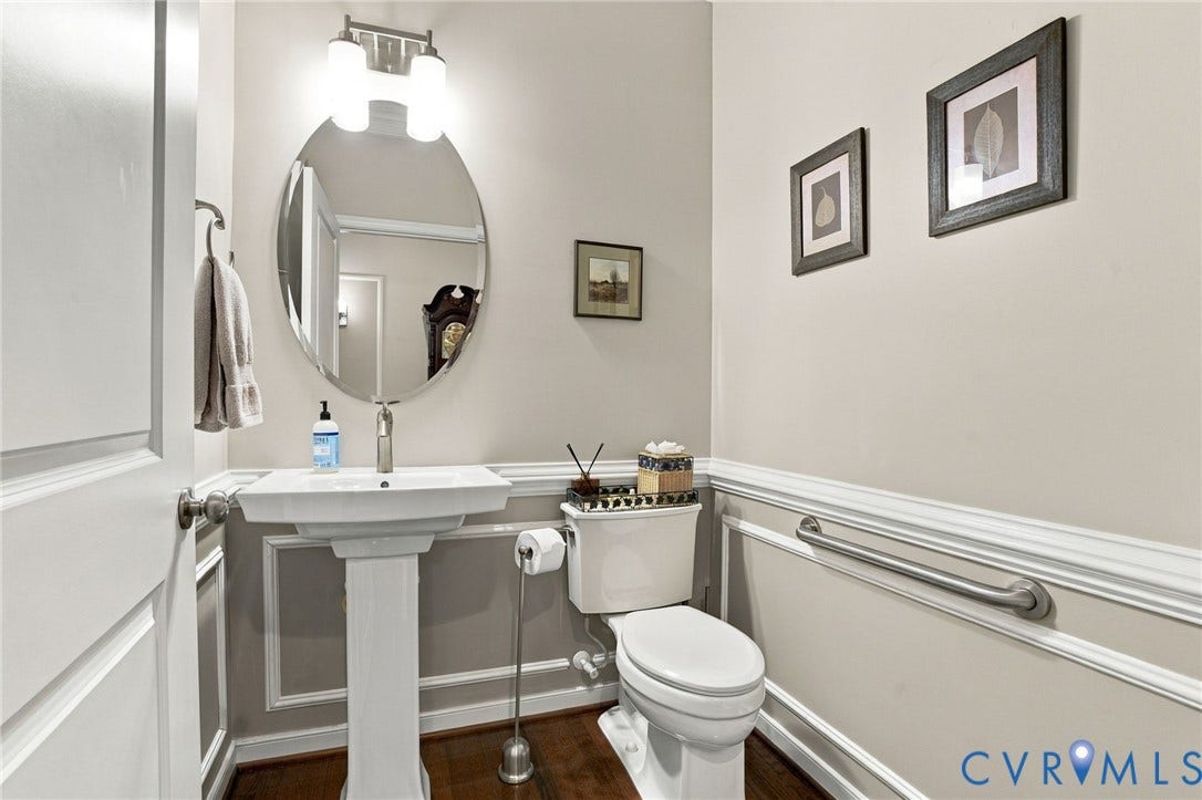 Pedestal sink with a polished chrome faucet, wall-mounted oval mirror, and a two-bulb vanity light fixture