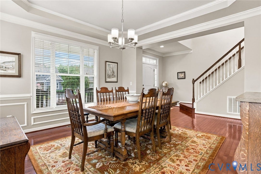 Tray ceiling with crown molding, wainscoting, large windows, wood-finish flooring, and a staircase with white balusters