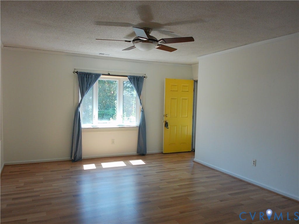 Wood-finish flooring, ceiling fan with integrated lighting, a bright yellow entry door, and a multi-pane window