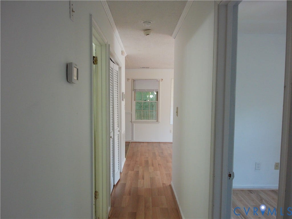 Hallway featuring wood-finish flooring, white walls, and a built-in thermostat