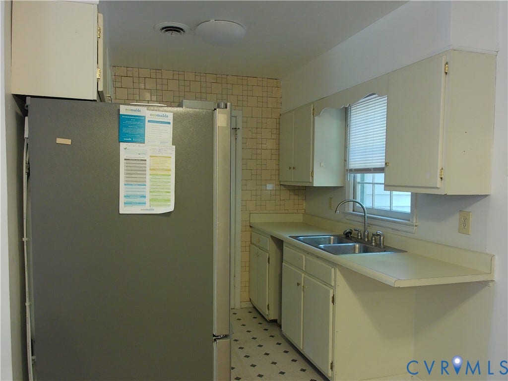 Kitchen featuring a double basin stainless steel sink, white cabinetry, light-colored countertops, and patterned floor tiling