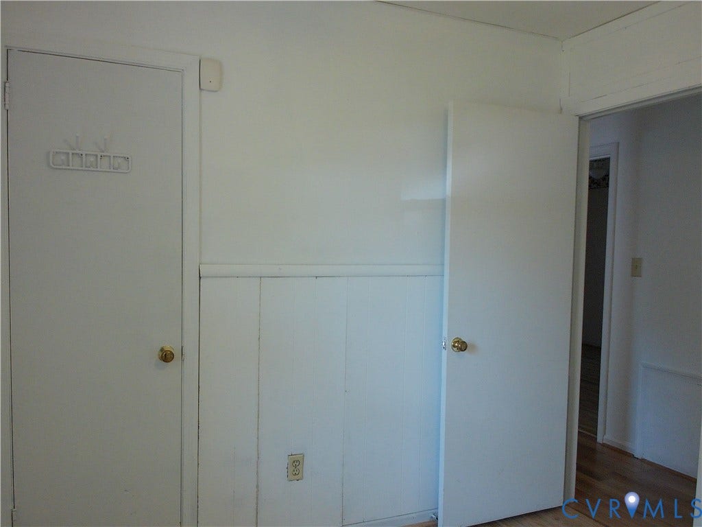 White wall paneling with a brass door knob and wood-finish flooring