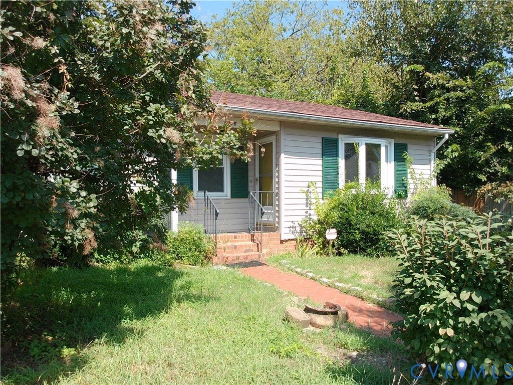 Single-story residence featuring light-colored siding, a dark roof, and green window shutters