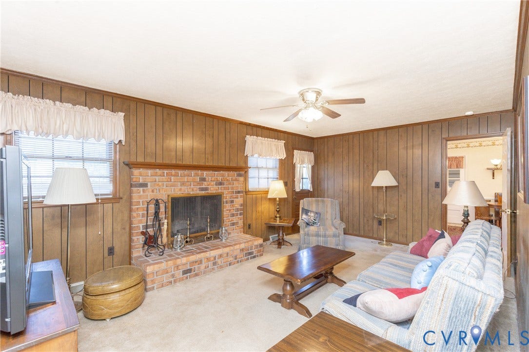 3640 Kiefer Road, Chester, VA 23831 Brick fireplace with hearth, wood paneling, light carpet flooring, ceiling fan, and multiple windows
