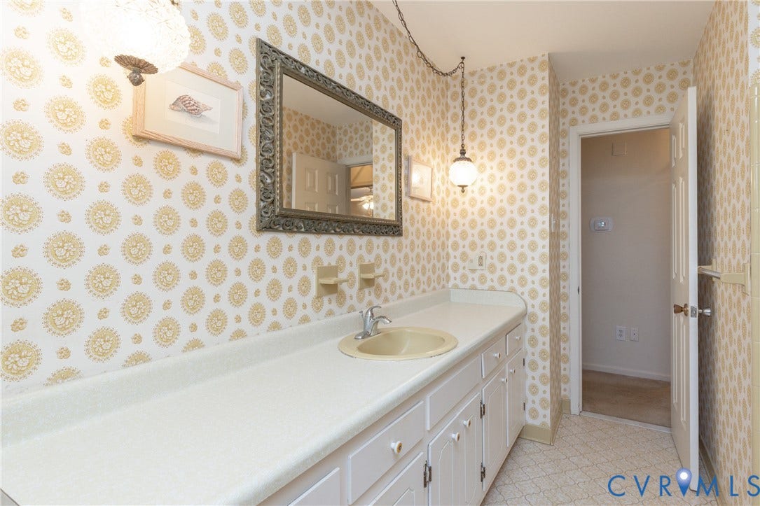 3640 Kiefer Road, Chester, VA 23831 Long vanity with integrated sink, ample storage cabinetry, decorative wall sconce, and patterned wallpaper