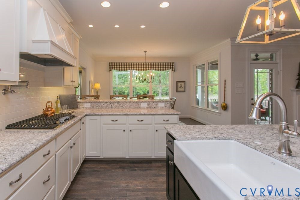 White cabinetry with dark pulls, stone countertops, wood-finish flooring, a built-in range hood, and a farmhouse sink with a gooseneck faucet