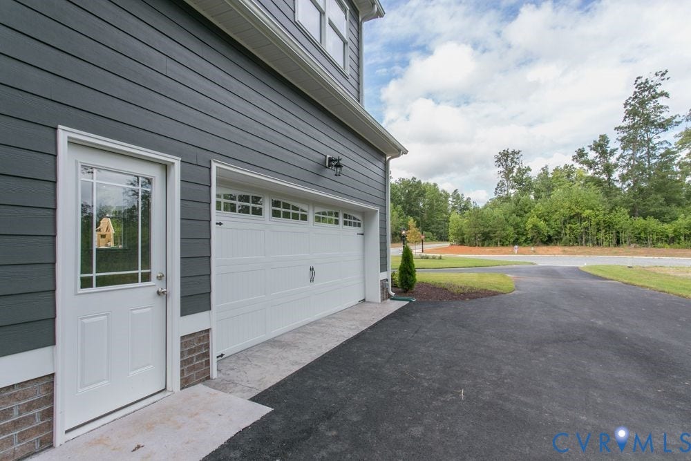 Gray horizontal siding, white garage door with window inserts, white entry door with divided lites, asphalt driveway, and concrete patio