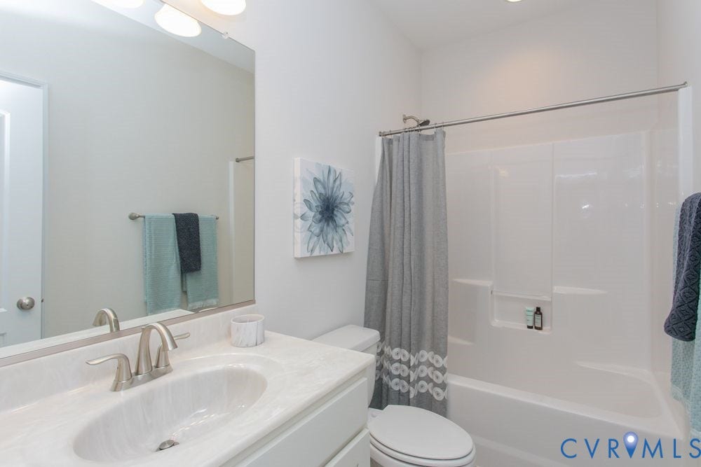 White vanity with an integrated sink, brushed nickel faucet, large wall mirror, white built-in bathtub, and a shower with a chrome showerhead