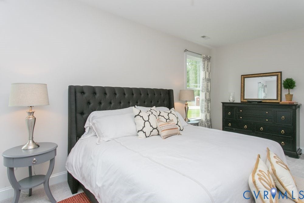 Brightly lit room featuring a window with patterned drapes, light-colored walls, and a tufted headboard