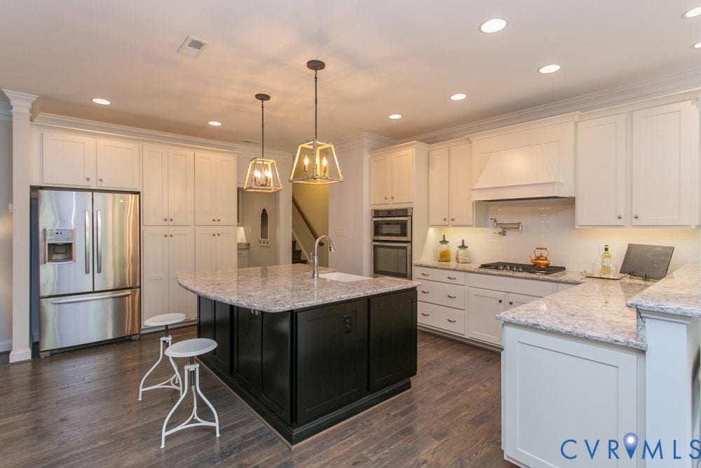 Kitchen featuring a large island with sink, stainless steel appliances, integrated wall oven and microwave, under-cabinet lighting, and wood-finish flooring
