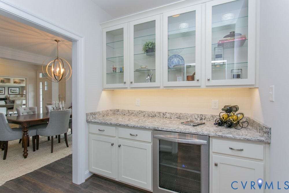 White cabinetry with glass-front upper units, light-toned countertop, integrated beverage cooler, and a tiled backsplash