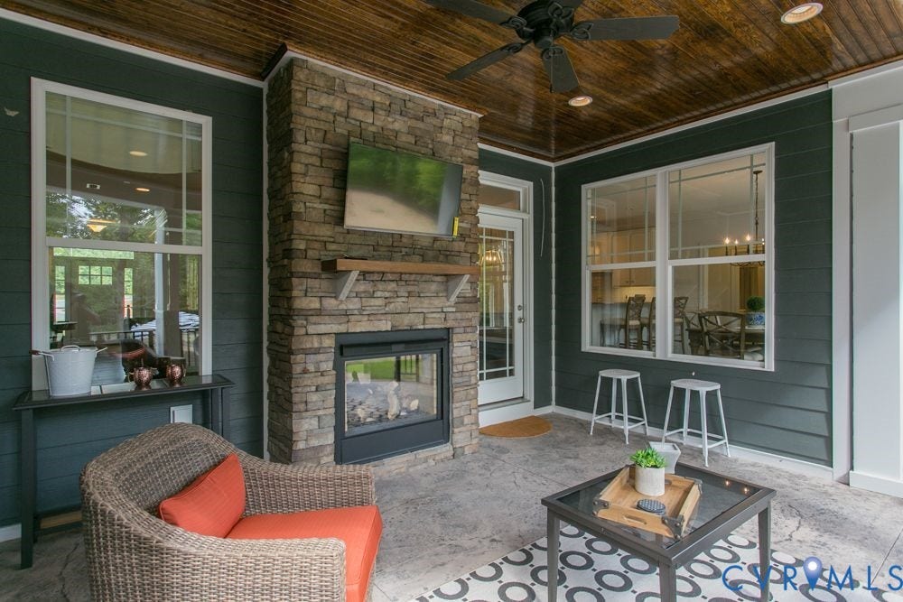 Stone-faced fireplace with a mantel, wood-finish ceiling with a ceiling fan, and large windows