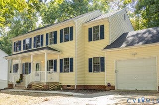 Two-story residence featuring light yellow siding, blue window shutters, an attached garage, a covered front porch, and a paved driveway