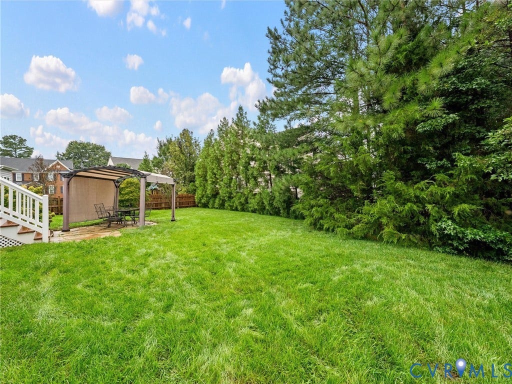 9990 Orchard Meadow Road, Mechanicsville, VA 23116 Expansive green lawn with mature perimeter trees, a white railing staircase, and a covered outdoor patio area